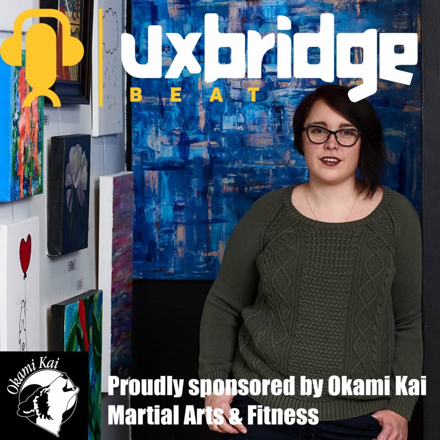 Sabrina Leeder, owner of Preston Art Gallery in Uxbridge, Ontario, surrounded by colourful original artwork. She is featured on the Uxbridge Beat podcast which is sponsored by Okami Kai Martial Arts and Fitness.